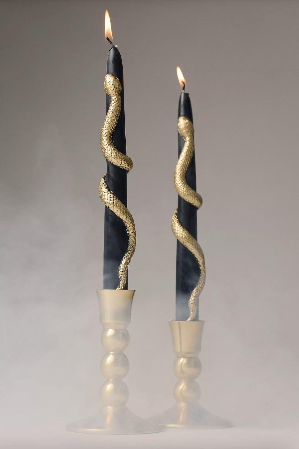 Two decorative candles with golden snake designs wrapped around them standing in gold candlesticks