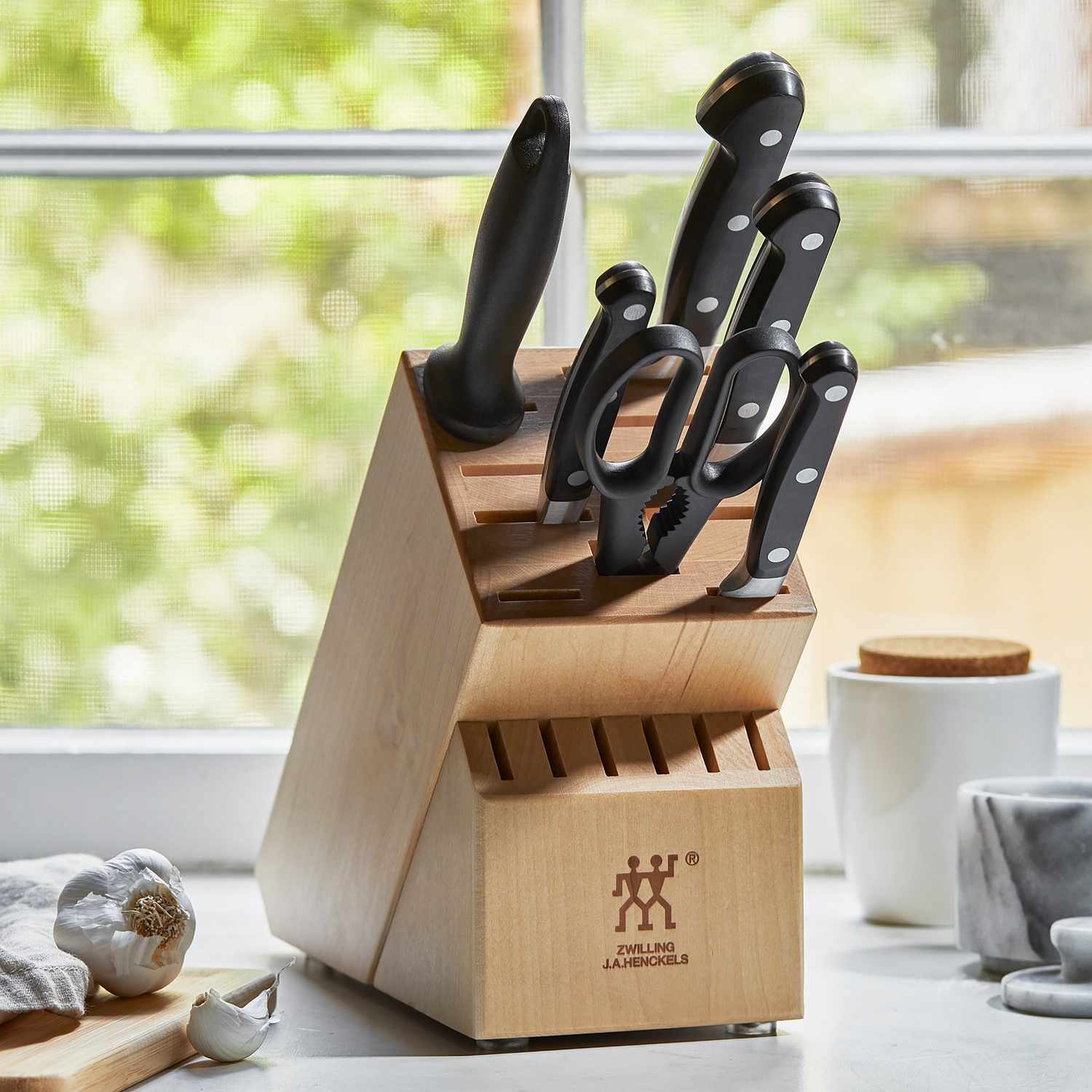 Wooden knife block holding various kitchen knives in a windowlit kitchen setting