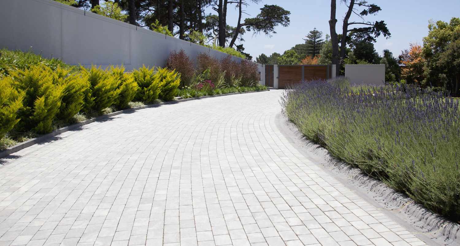 A curved cobblestone driveway lined with plants and leading to a gate
