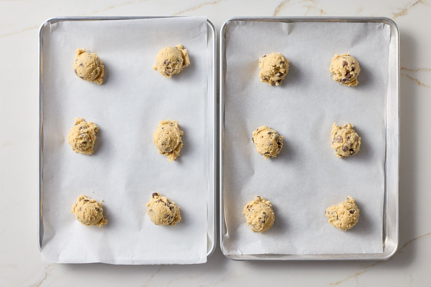 Two trays with cookie dough scoops on parchment paper ready for baking