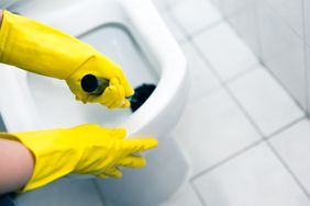 Person cleaning a toilet with a brush hands wearing yellow rubber gloves