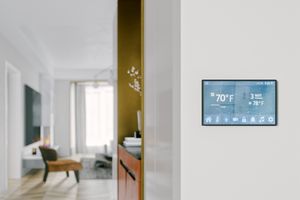 Smart thermostat mounted on a wall showing temperature and settings view of a modern living space in the background