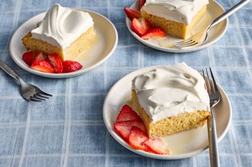 portions of tres leches cake topped with whipped cream, with strawberries on the side