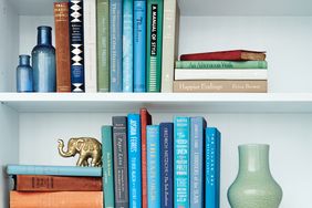 A styled shelf with books decorative glass bottles a gold elephant figurine and a vase