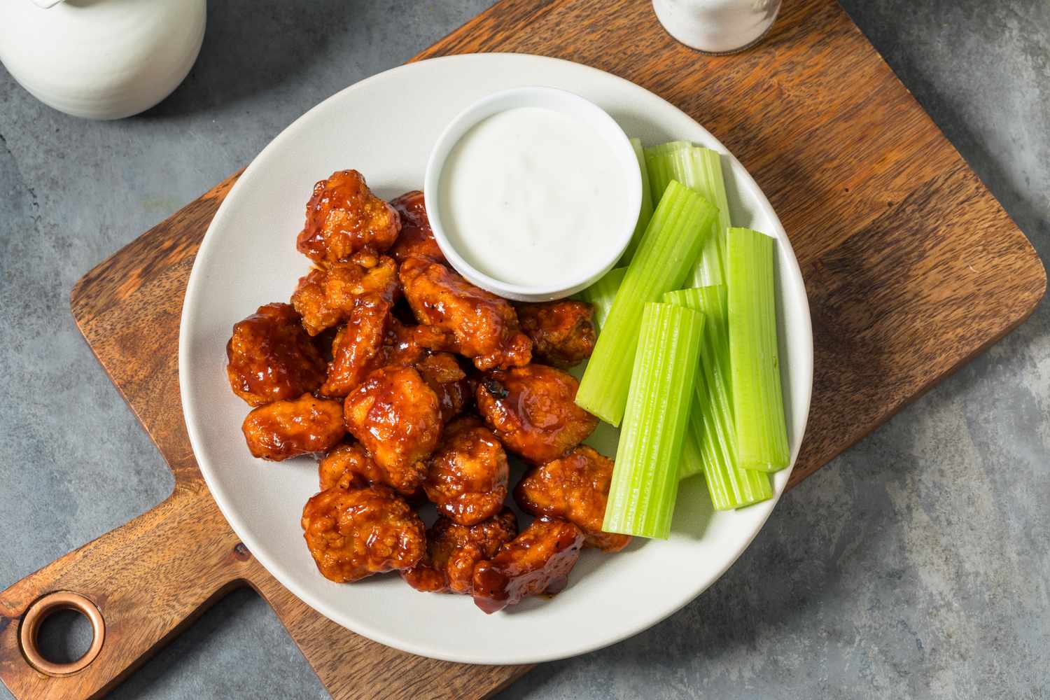 A plate with buffalo wings celery sticks and a cup of dipping sauce on a wooden board