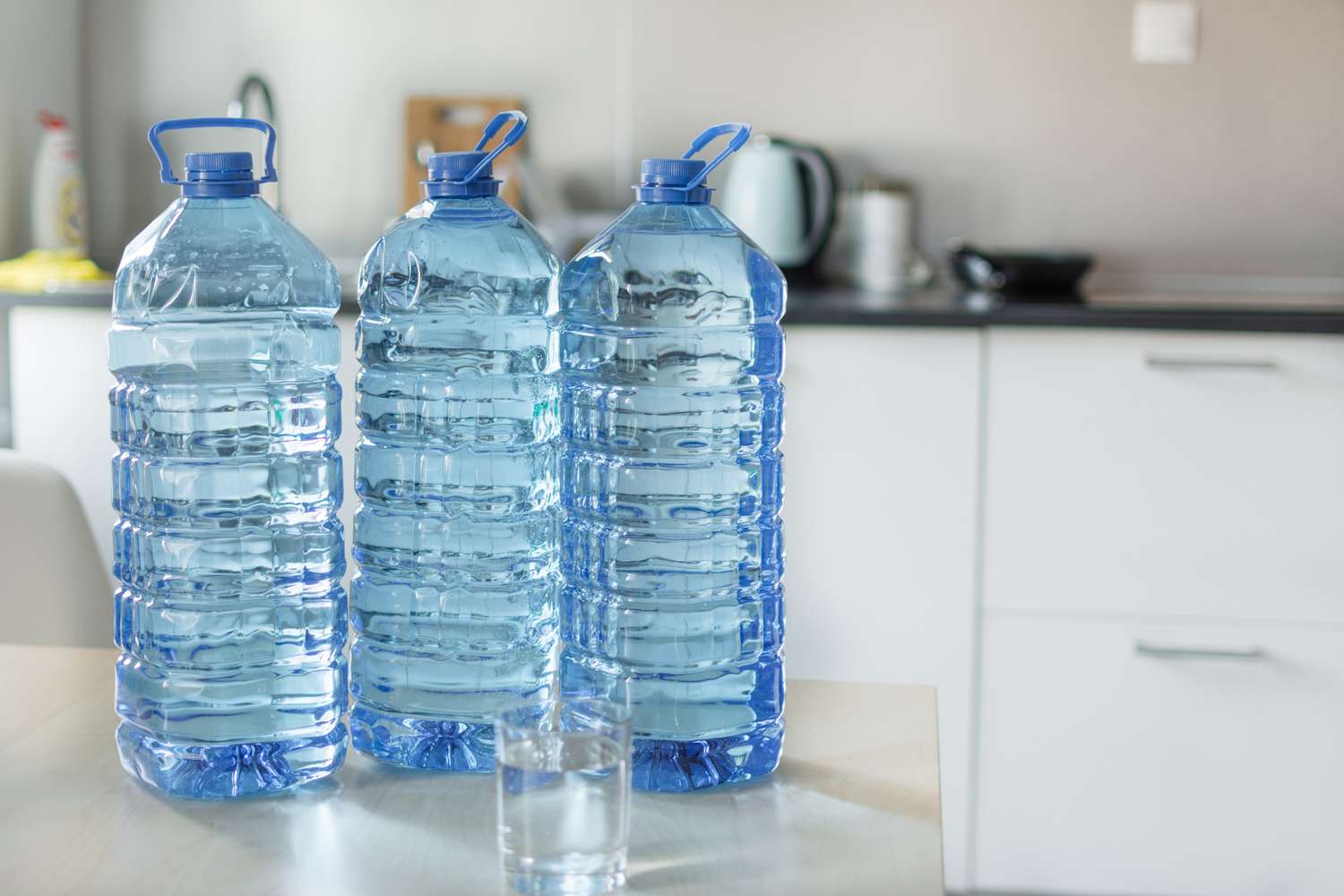 Three large water bottles and a glass on a kitchen counter