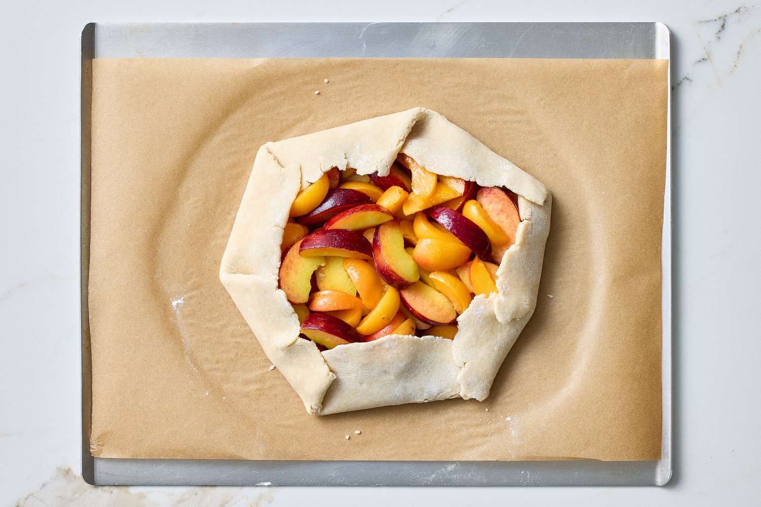 Unbaked fruit galette on a parchment-lined baking sheet, featuring sliced stone fruit