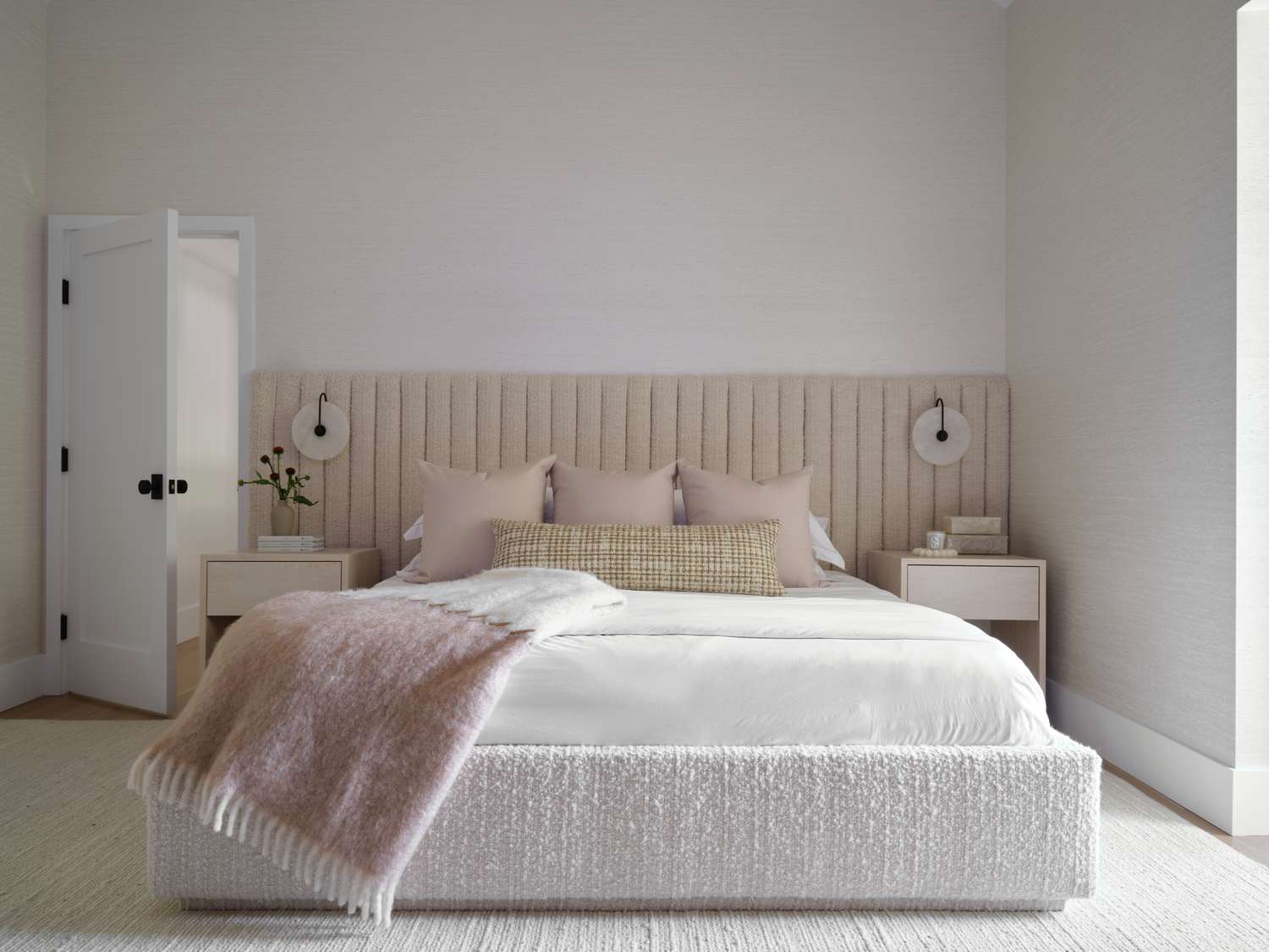 a neutral primary bedroom with king bed and wall to wall headboard and pale pink pillows