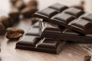 Closeup of stacked chocolate bars on a wooden surface surrounded by cocoa beans