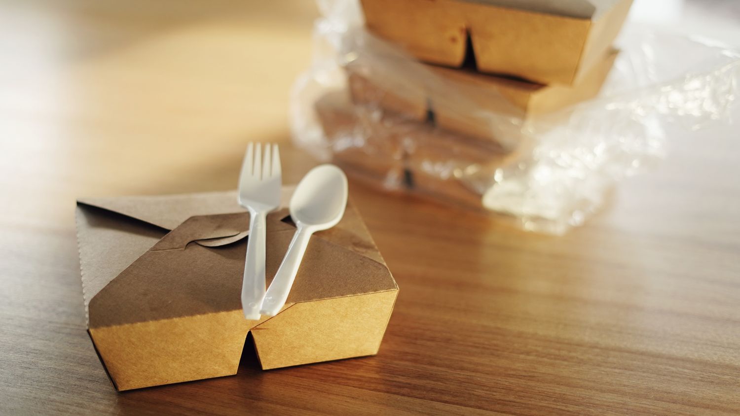 Several disposable food containers stacked with a plastic fork and spoon on top placed on a wooden table