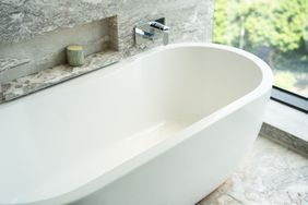 A modern freestanding bathtub with a view of a garden through a nearby window