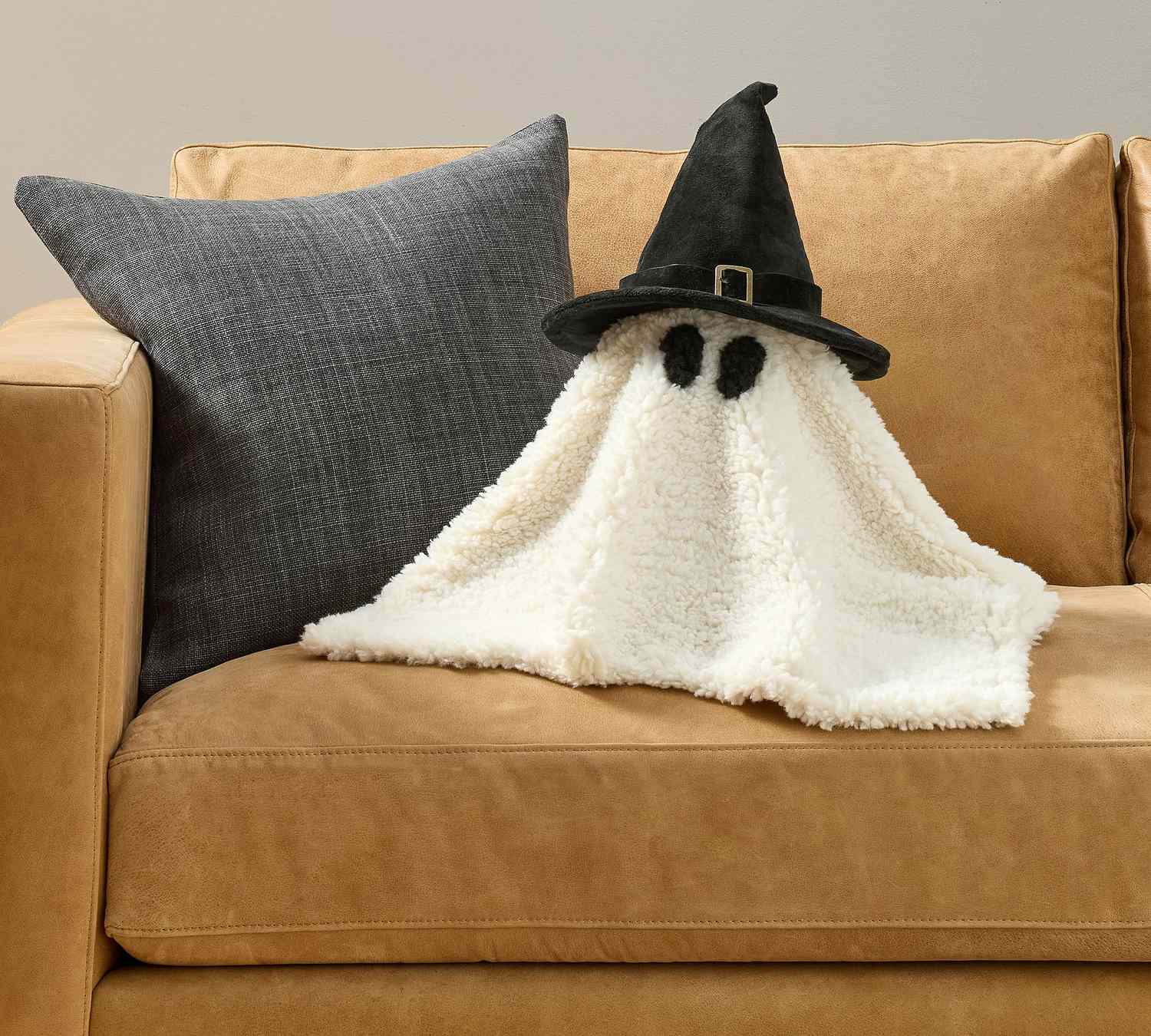 A ghostshaped decorative item with a witch hat placed on a couch next to a pillow