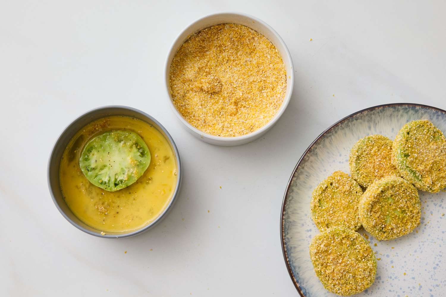 Green tomato slices being prepared shown with egg wash breading and breaded slices on a plate