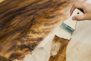 A hand applying wood finish with a brush on a wooden surface