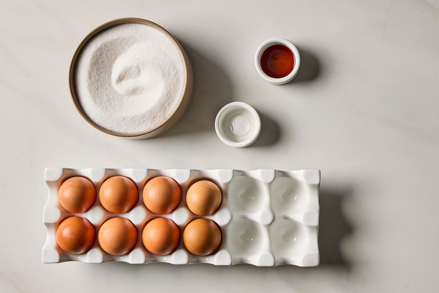 Ingredients including eggs sugar vanilla and cream of tartar arranged on a countertop