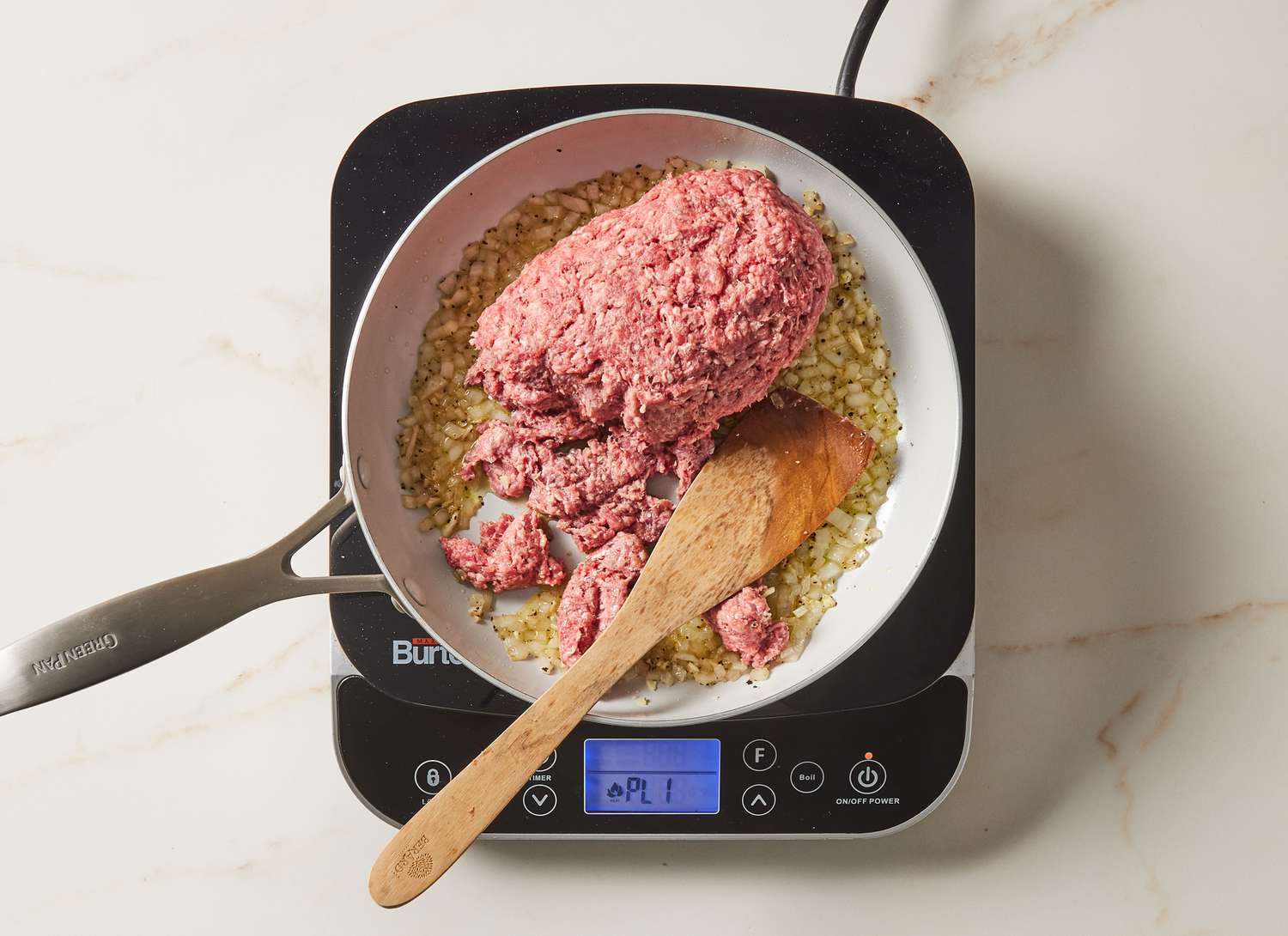 onions and ground beef sautÃ©ing in a skillet with a wooden spoon