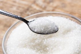 A spoon holding granulated sugar above a bowl of sugar
