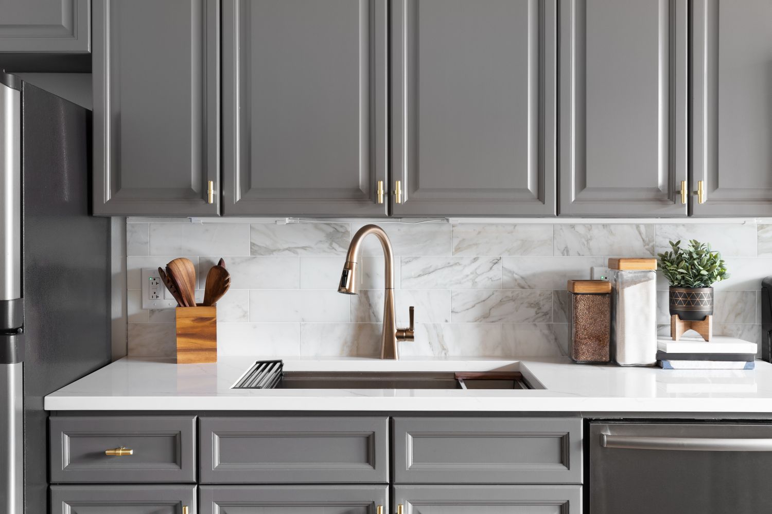 A kitchen with grey cabinets a marble backsplash and a sink with a faucet