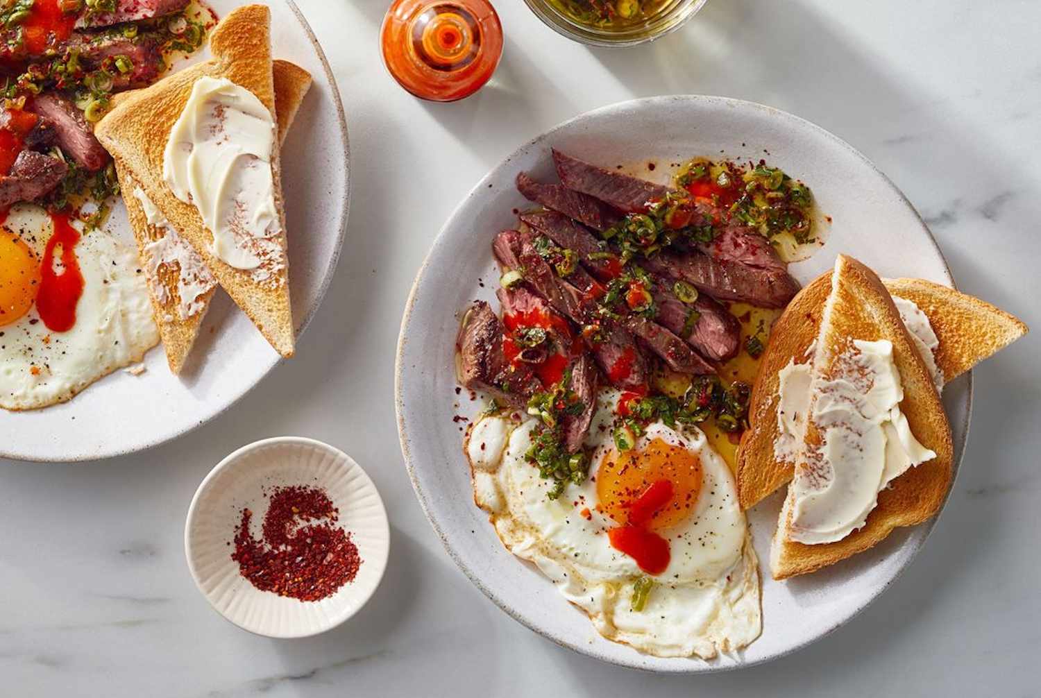 Plates with steak fried eggs toast and condiments on a table
