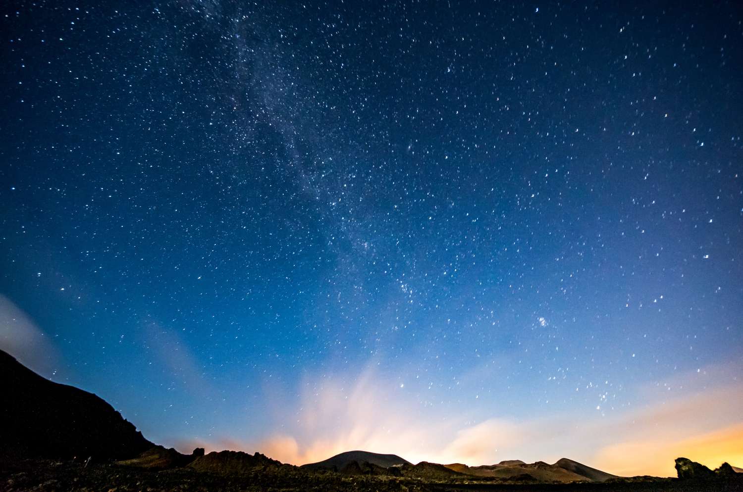 Starry night sky with a luminous horizon over silhouetted mountains