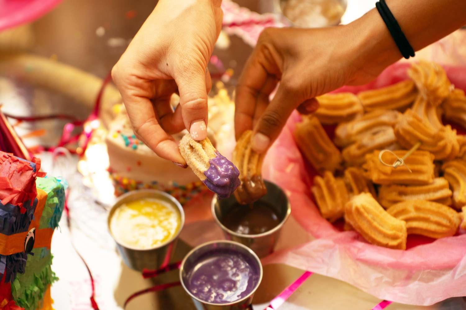 Hands dipping churros into colorful sauces with a basket of churros nearby