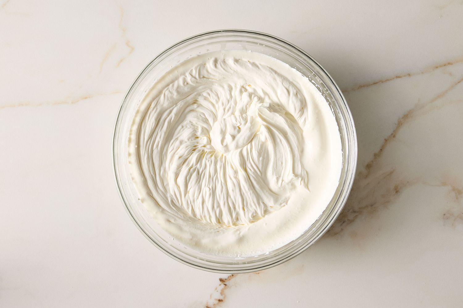 A bowl of whipped cream seen from above on a light countertop surface
