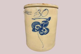 A beige ceramic crock with a blue floral design and the number 30 inscribed on it includes text indicating a maker or origin