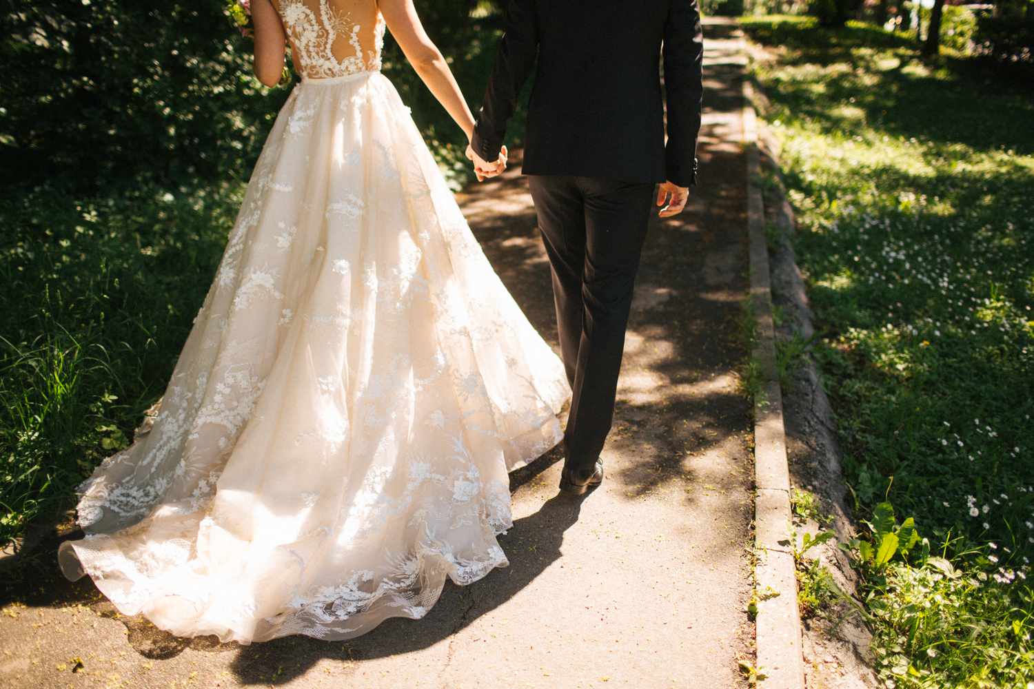A bride and groom holding hands while walking along a pathway