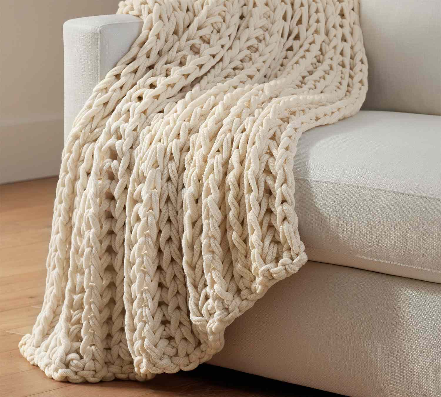 A chunky knit throw draped over the arm of a sofa