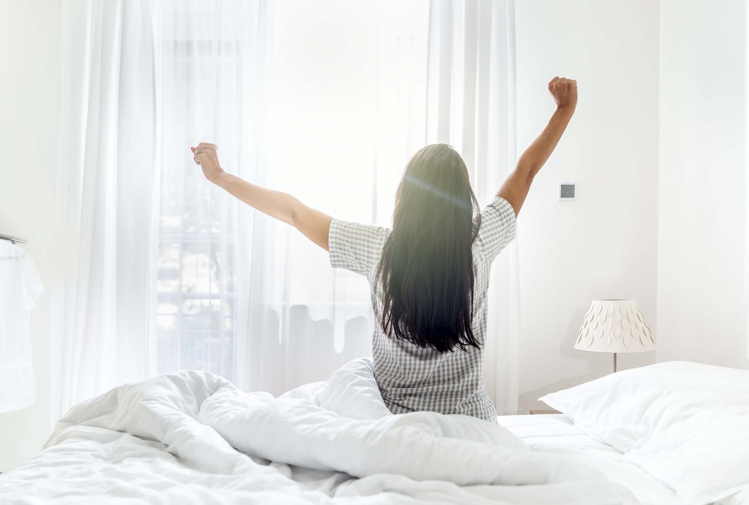 Person stretching while sitting on a bed in a bright room