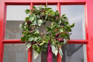 green wreath with berries and floral accents hanging on red door