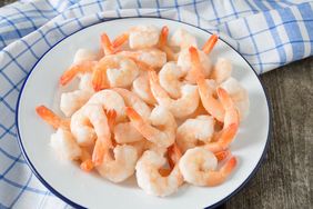 A plate of cooked shrimp with tails arranged on a white dish on a surface with a checkered cloth