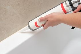 Hands applying caulk to the edge of a bathtub using a caulking gun
