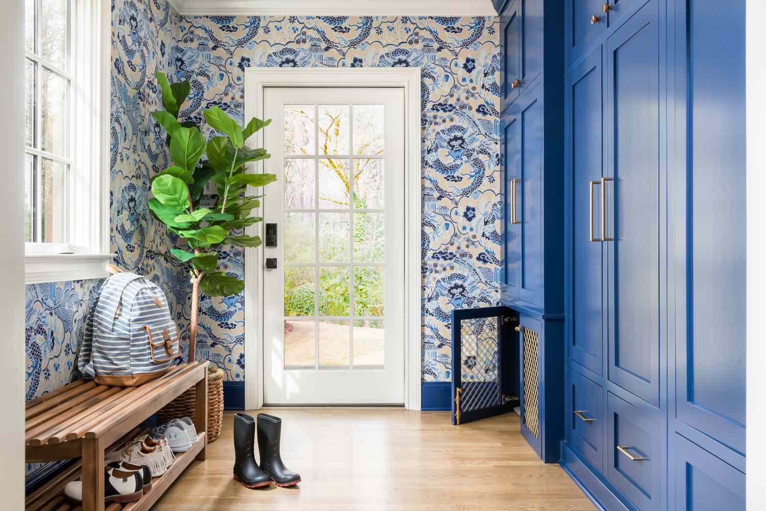 A mudroom with blue cabinets a bench with items on it and a glass door