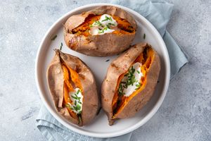 Plate with three baked sweet potatoes topped with sour cream and chopped chives placed on a light cloth