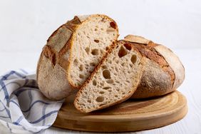 A sliced loaf of sourdough bread on a wooden board a cloth napkin beside it