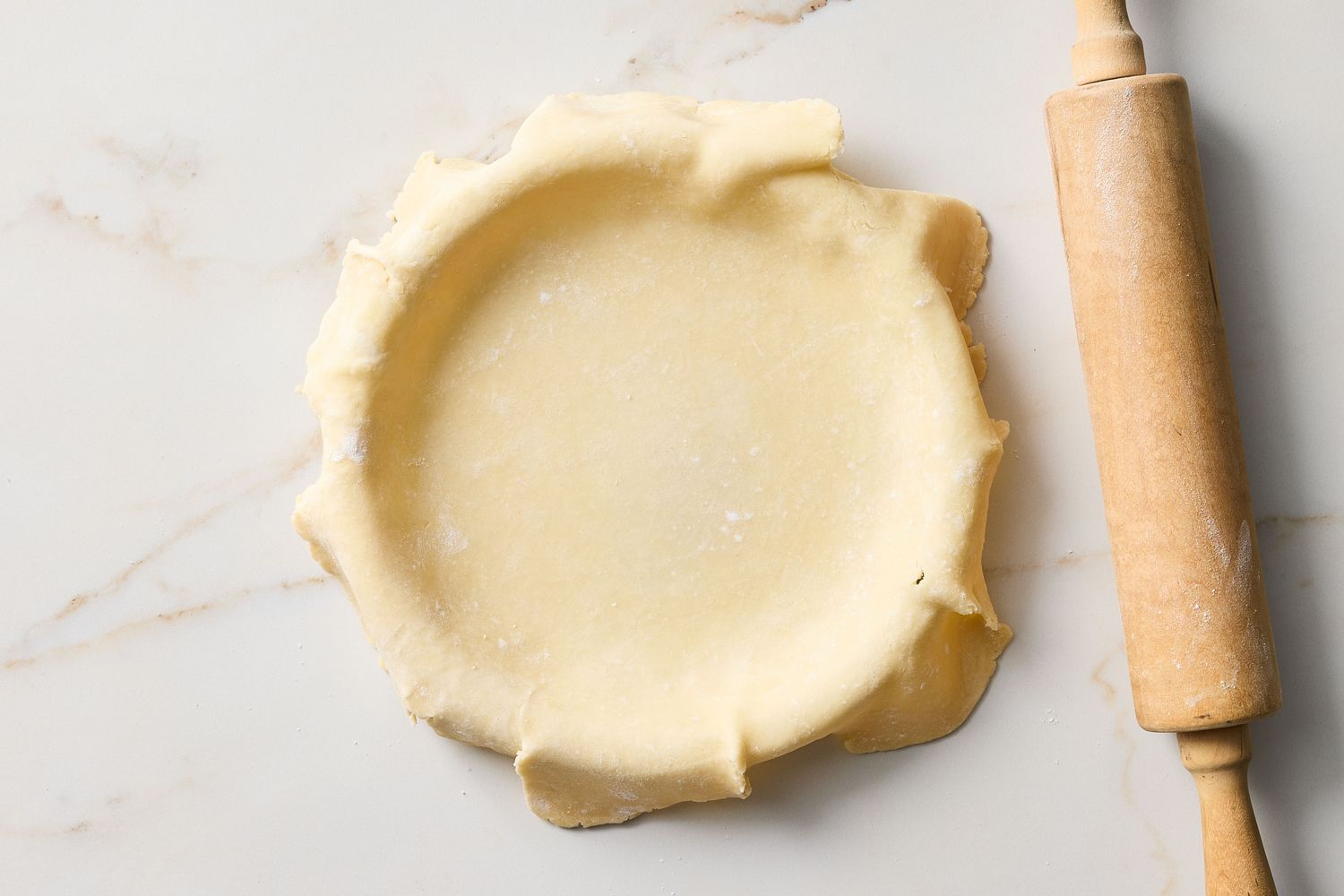 Pie crust placed in a round dish with a rolling pin on the side