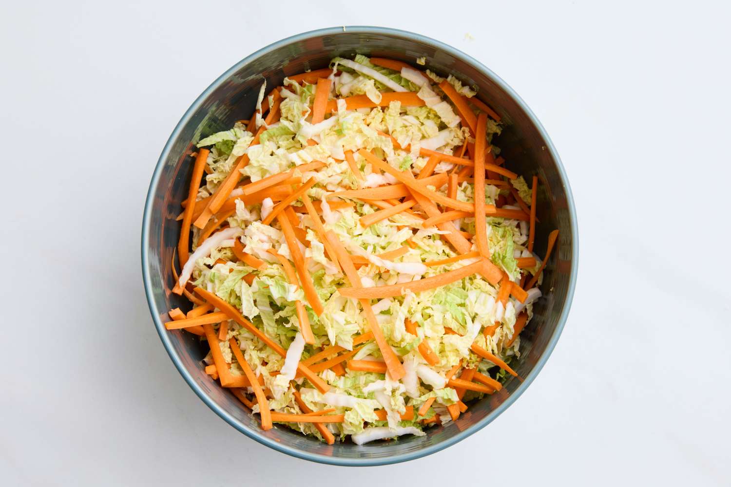 A bowl of napa cabbage slaw with shredded carrots and greens