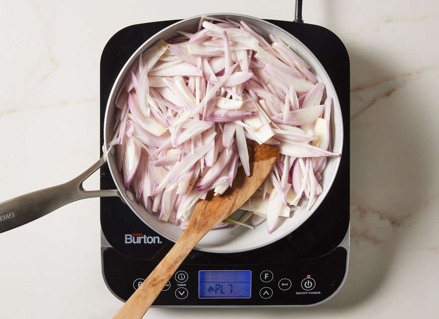 sliced shallots in a pan with a wooden spoon