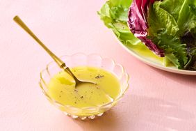 A bowl of vinaigrette with a spoon next to a plate of mixed greens