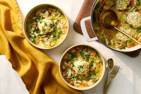 Bowls and a pot of chicken and dumplings with a serving ladle and utensils on a table with a yellow cloth