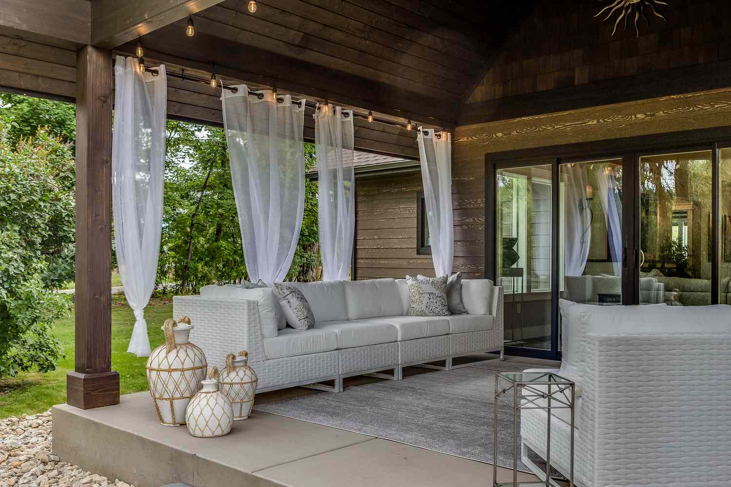 A covered outdoor seating area with sofas, curtains, and decorative lanterns on a patio