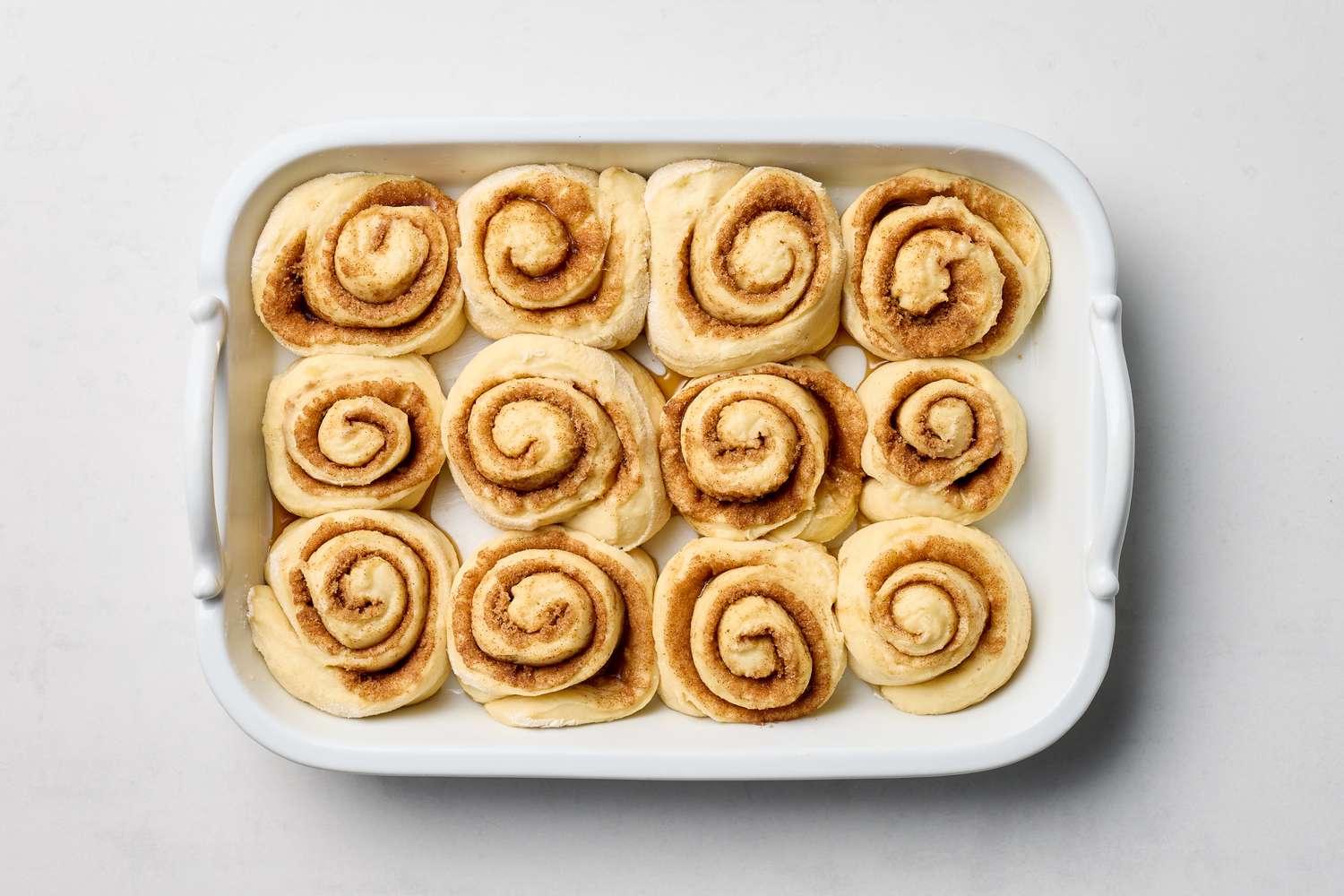 A baking dish containing twelve uncooked cinnamon rolls arranged in rows