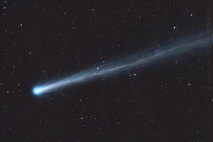 A comet streaking across a starfilled night sky showing a bright nucleus and a long tail extending to the right