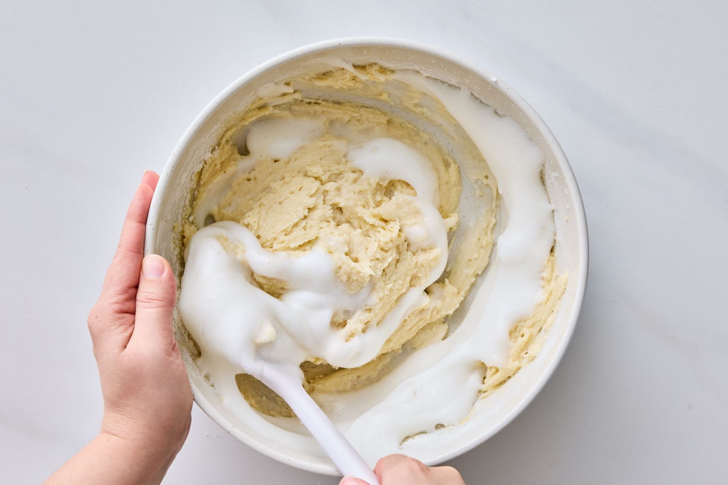 A person stirring cake batter in a bowl using a spatula