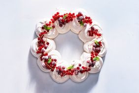 A pavlova dessert arranged in a circular wreath topped with red berries and mint leaves