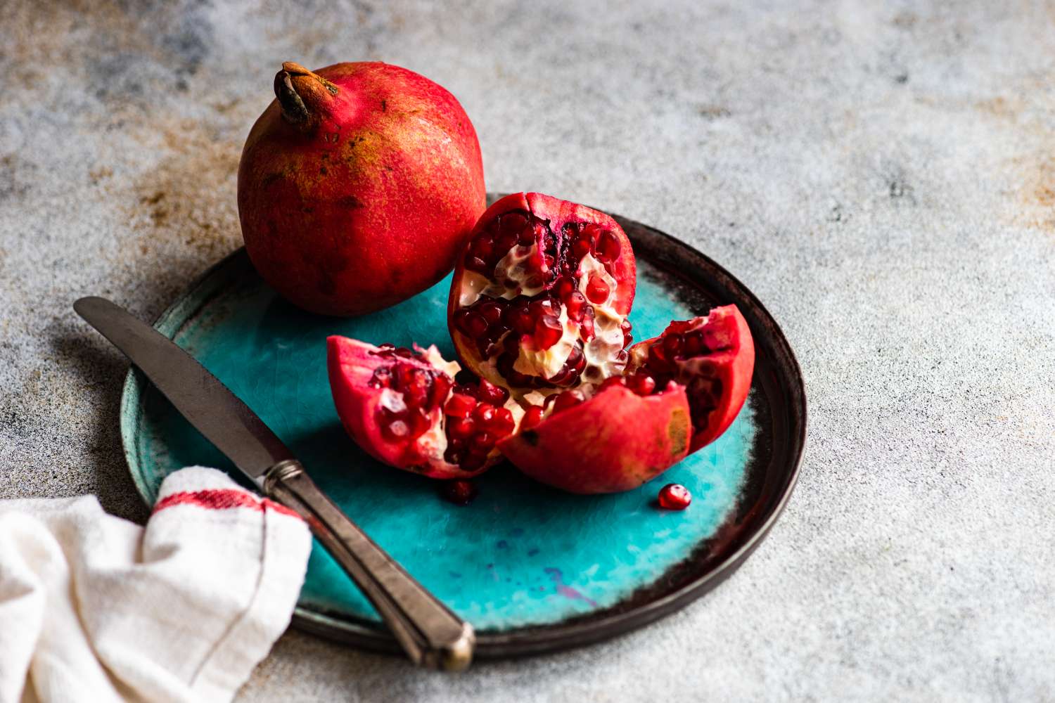 one whole pomegranate and one broken into quarters on a blue plate with a knife