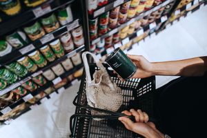 Person holding a canned item in a supermarket placing it into a shopping basket