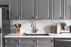 A kitchen with grey cabinets a marble backsplash and a sink with a faucet
