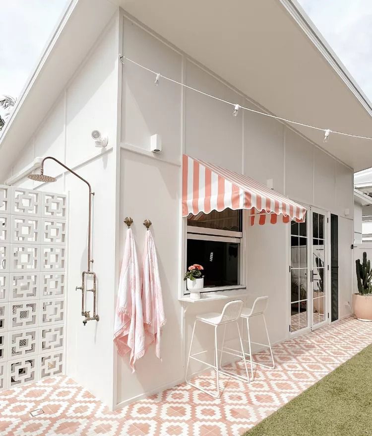 Light and airy outdoor shower with pops of light pink striped awning and pink tiles.